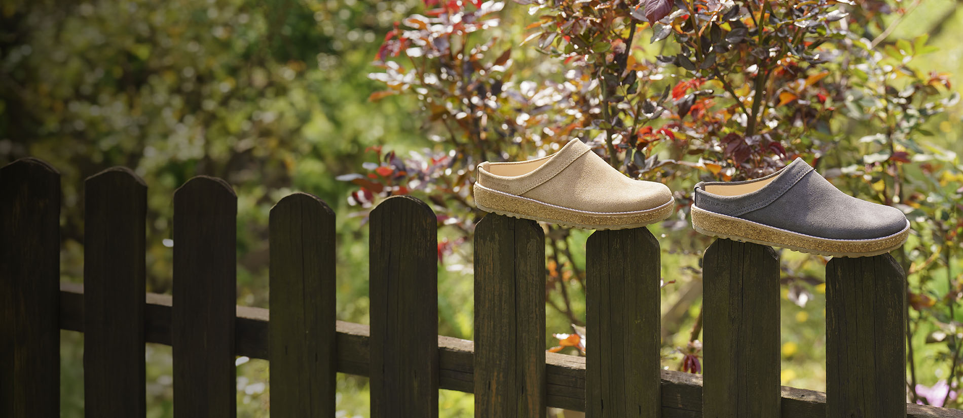 ciabatte sabot in pelle liscia haflinger travel marroni e nere appoggiate su staccionata in legno