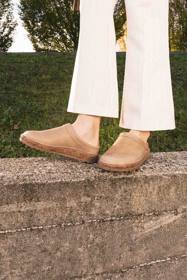 Primo piano di sabot in pelle di haflinger indossato da persona con pantaloni bianchi in piedi su un muretto