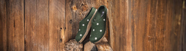 Primo piano di sabot haflinger in lana con ricami margherite appoggiate su una pila di tronchi e su un muro di legno