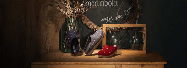 pantofole sabot haflinger con ricami cuoricini in tre colorazioni blu. grigio e rosso su mobile in legno