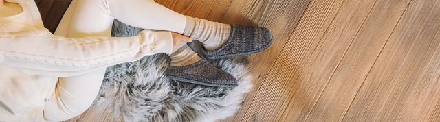 Vista dall'alto di pantofole haflinger in lana tricotè color jeans indossate da donna sdraiata su tappeto