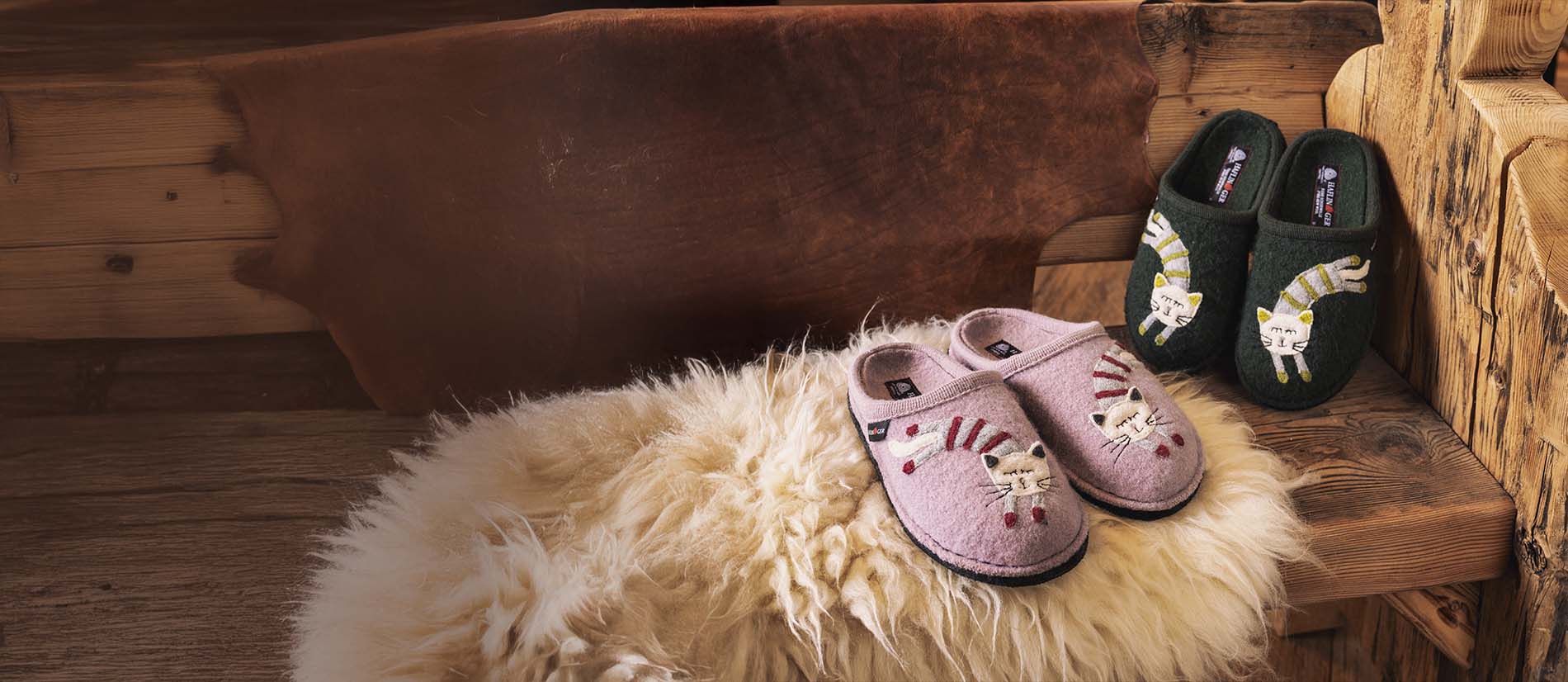 Primo piano di pantofole haflinger choupette rosa e verdi appoggiate su una panca di legno 
