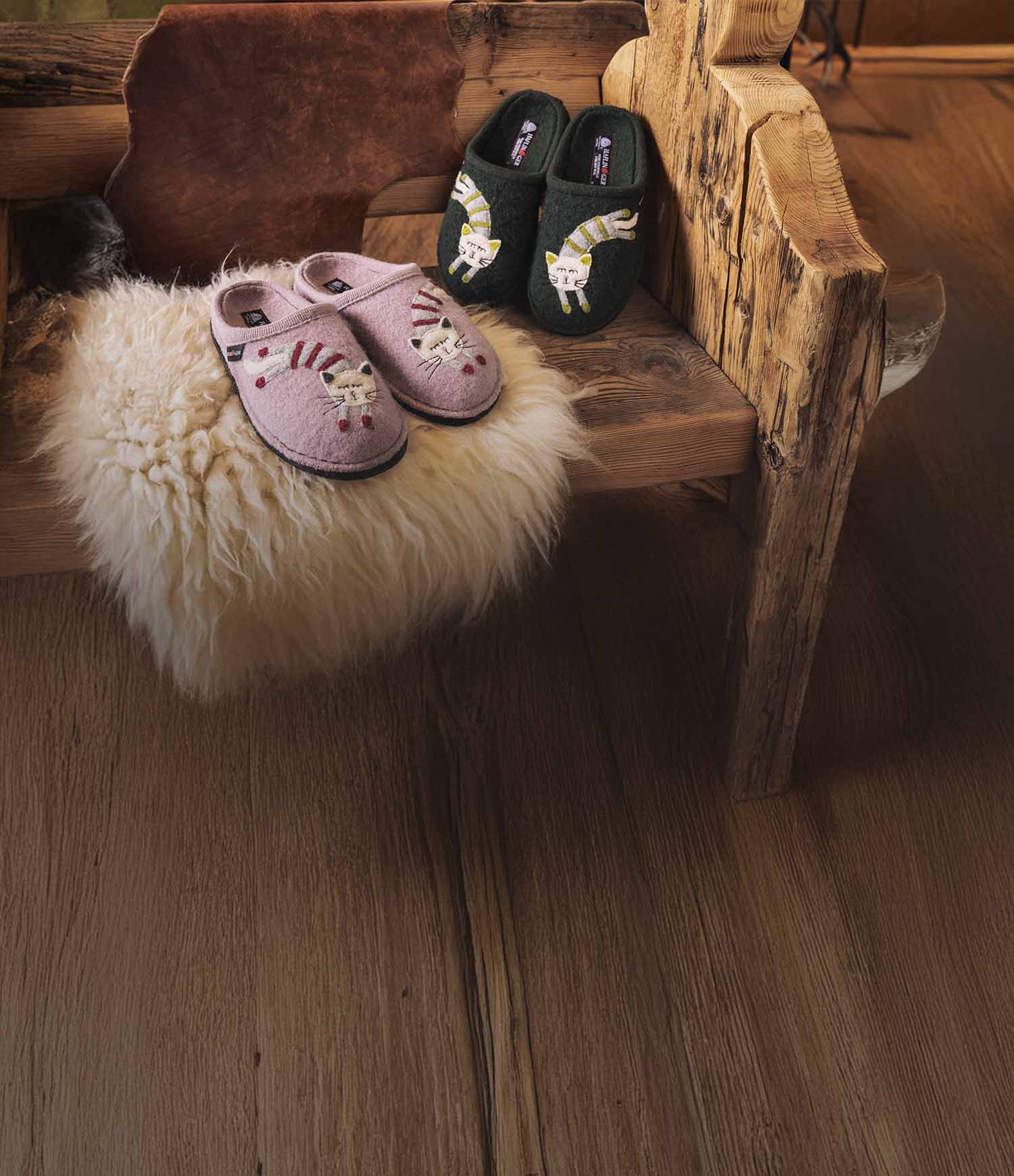 Pantofole haflinger choupette rosa e verdi con ricamo di un gatto appoggiate su una panca di legno 