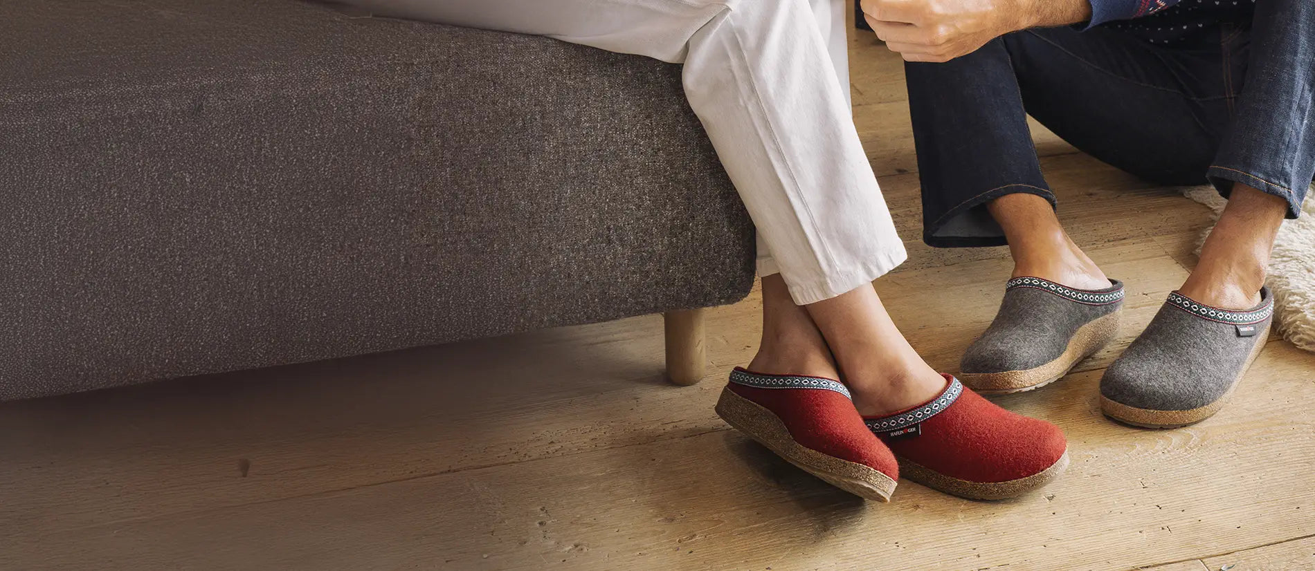 Primo piano di due paia di franzl, una paio rosse indossate da donna seduta su divano e un paio grigie indossate da uomo seduto su pavimento di legno