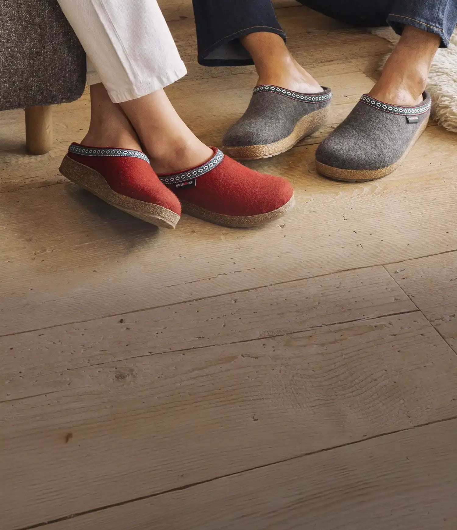 Primo piano di franzl rosse rubin indossate da donna seduta una poltrona e un paio di franzl grigie indossate da uomo seduto su un tappeto