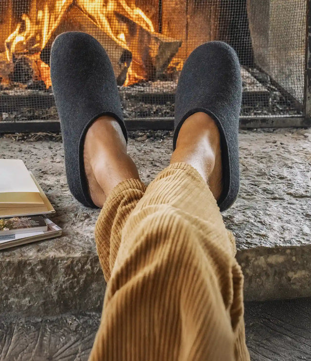 Primo piano di Fundus Sabot Unisex graphit indossate da uomo con piedi appoggiati vicino ad un caminetto acceso
