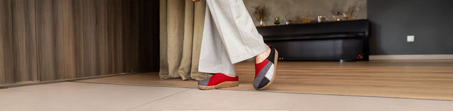 Primo piano di Haflinger Patchwork Sabot unisex rubin in feltro di pura lana vergine con plantare anatomico in sughero e lattice e suola antiscivolo in termorubber indossato da persona con pantaloni larghi grigio chiaro.